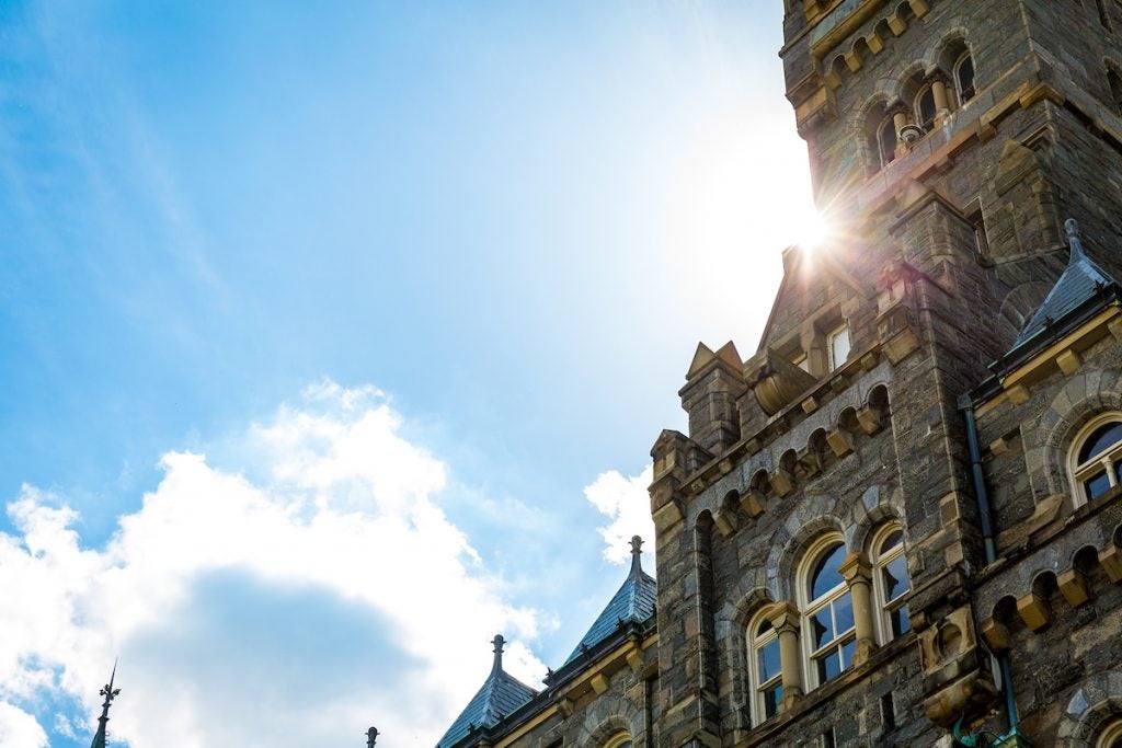 An image of Healy Hall with a sun flare peeking out from behind the clock tower