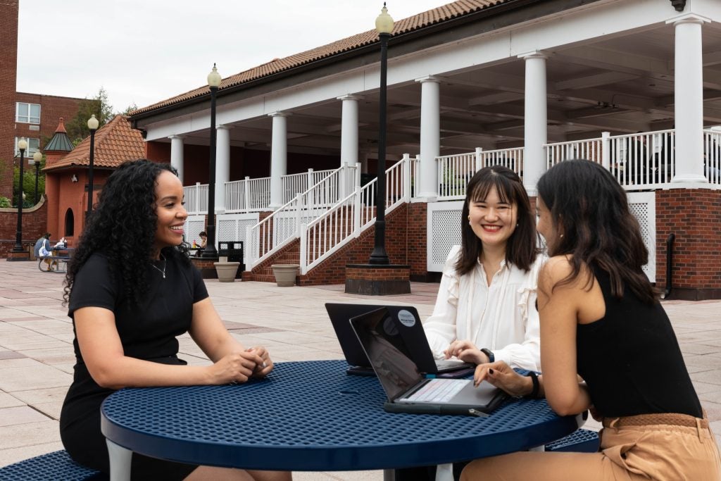 Two graduate students sit at a round picnic table with a faculty mentor