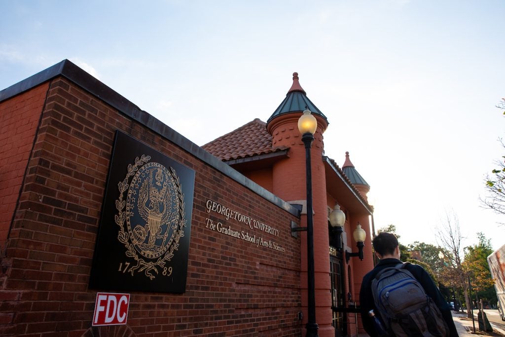 Student walks in front of the Graduate School of Arts & Sciences sign on the Car Barn building at Georgetown